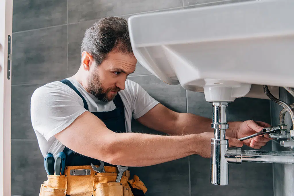 Middle-aged plumber hard at work under a sink.