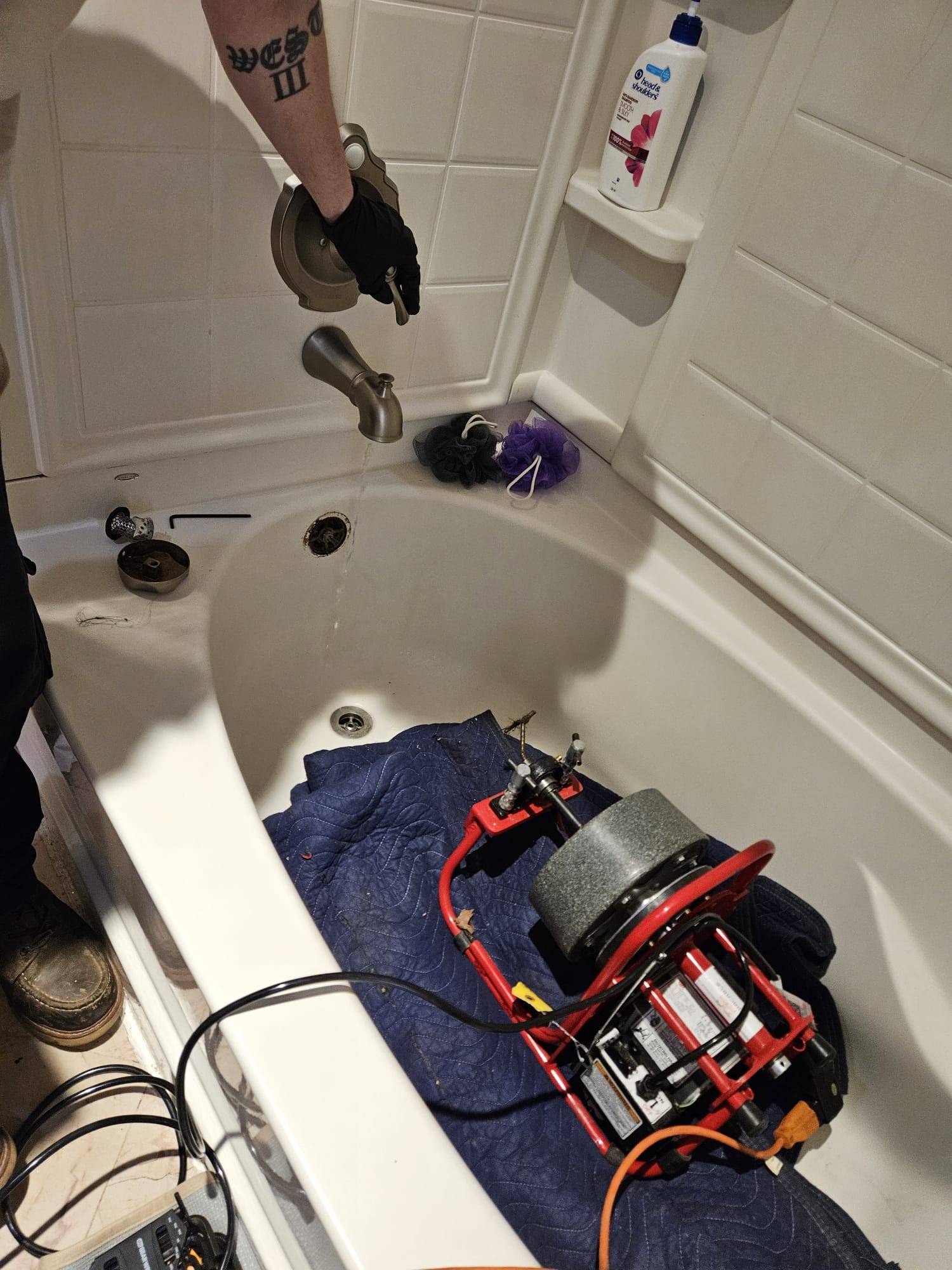 Person using a drain snake to clear a clogged bathtub drain through the overflow opening